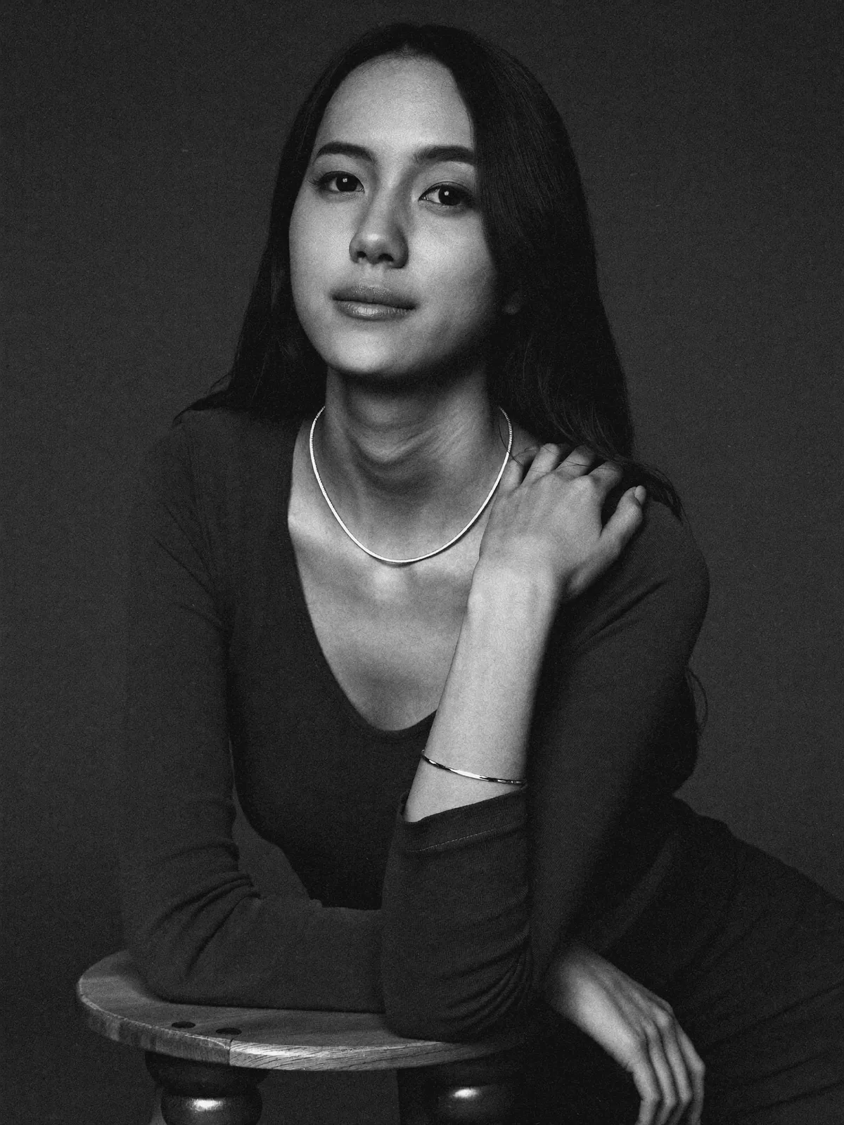 Seated editorial black-and-white portrait, a slim silver chain and a bangle