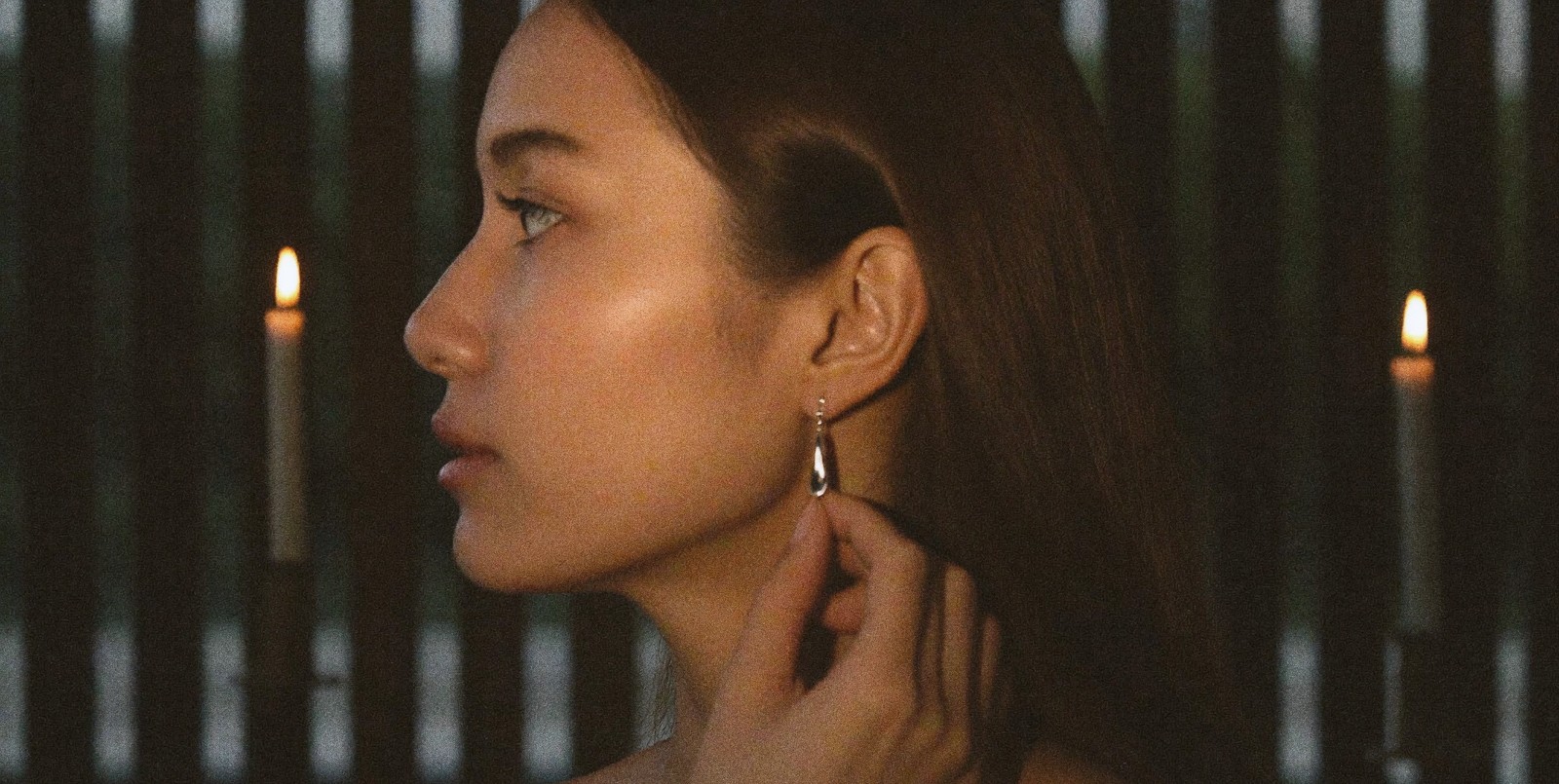 A candlelit profile, a sterling silver teardrop drop earring catching the flame