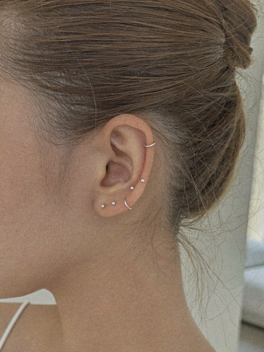 A curated ear in warm daylight — three sterling silver lobe studs, a fine huggie and a helix cuff