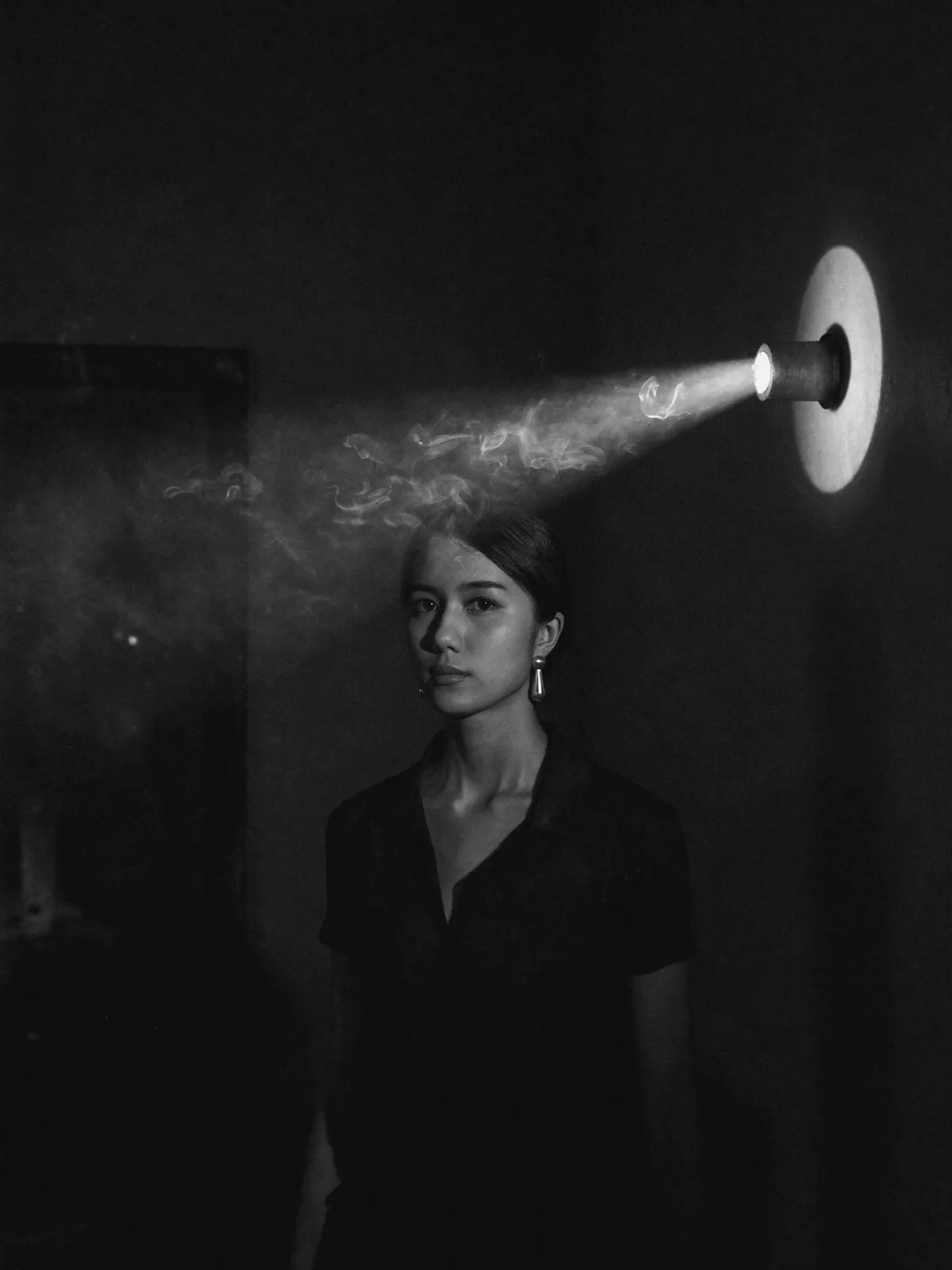 Spotlight and drifting smoke across a woman's face, a silver teardrop earring glinting in the beam